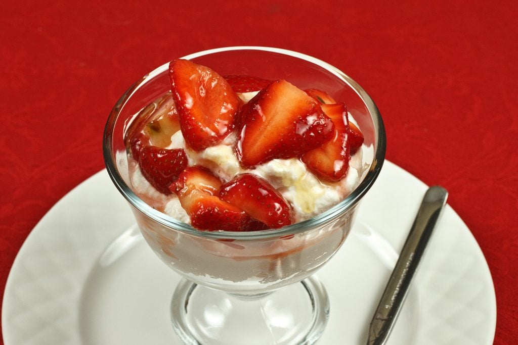 glass dish of honey ricotta mousse with strawberries sitting on a white plate