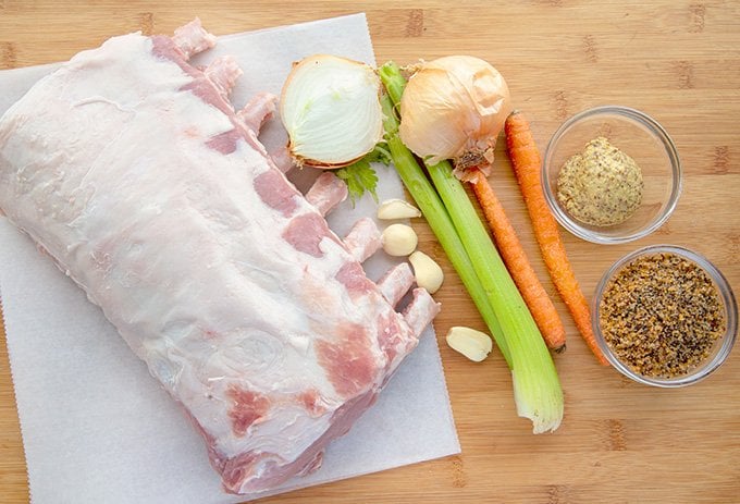 raw bone in rack of pork with seasonings  and vegetables on a wooden cutting board