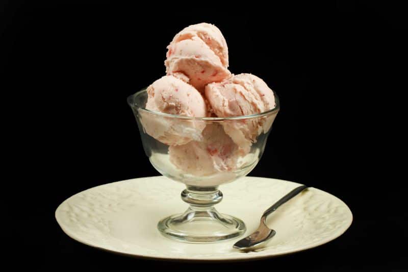 scoops of strawberry ricotta gelato in glass dish on a white plate with a spoon