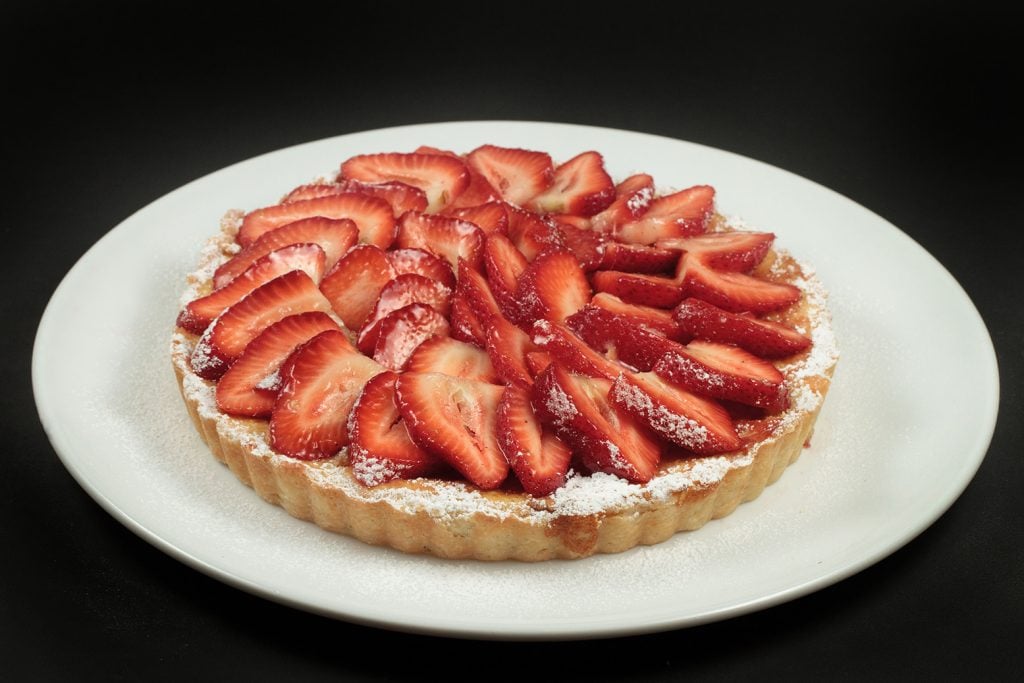 strawberry ricotta crostata on a white plate on a black background