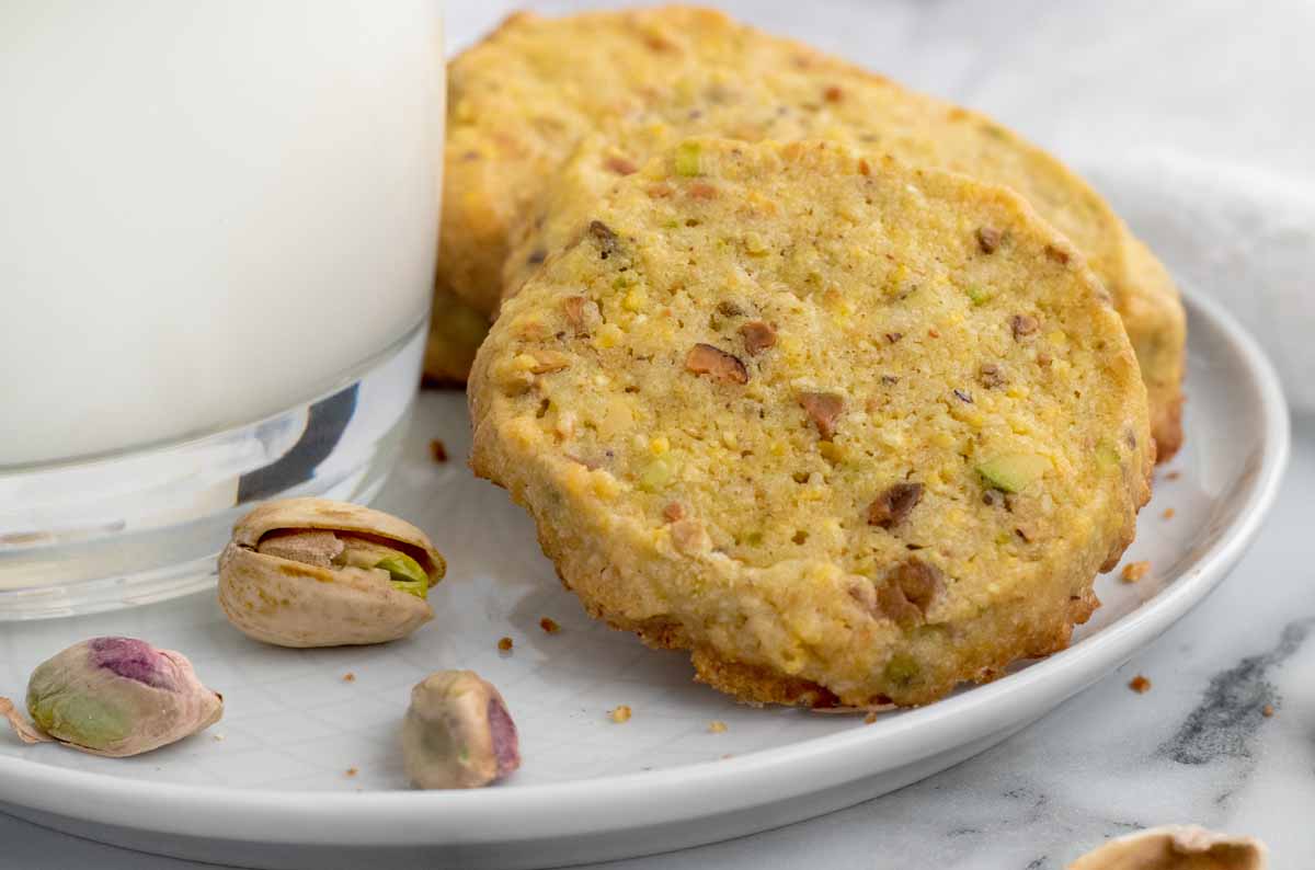 pistachio cookies on a white plate with a glass of milk