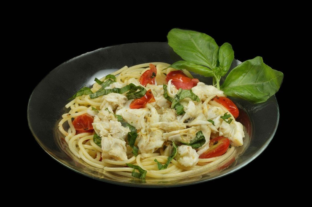 A black bowl of pasta topped with jumbo lump crabmeat, basil and tomatoes 