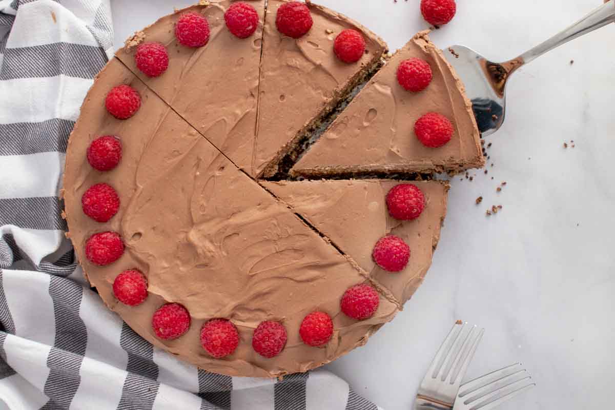 overhead view of whole cheesecake topped with raspberries with a slice being taken out on a spatula 