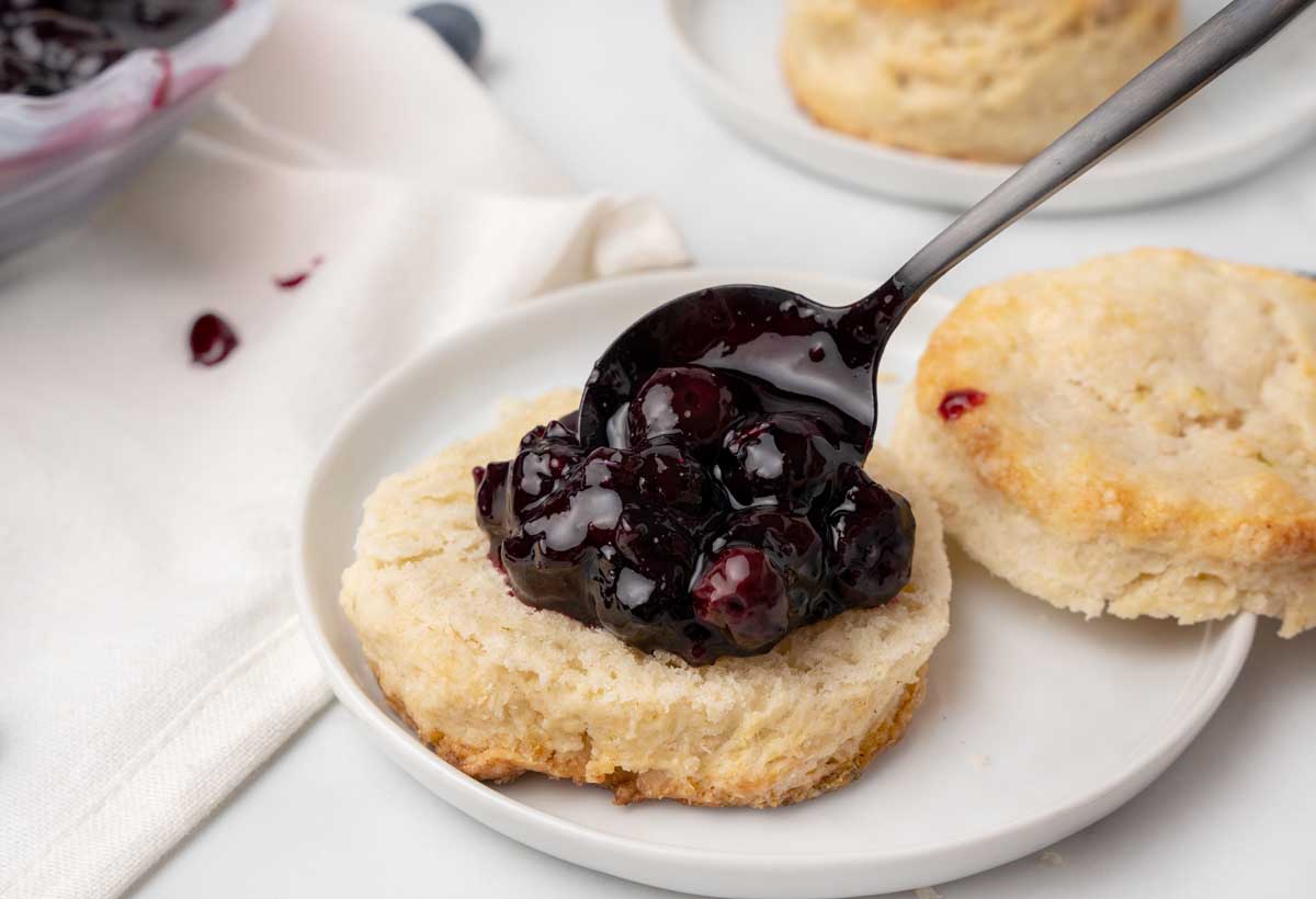 spooning blueberry compote on the bottom of a sliced scone.