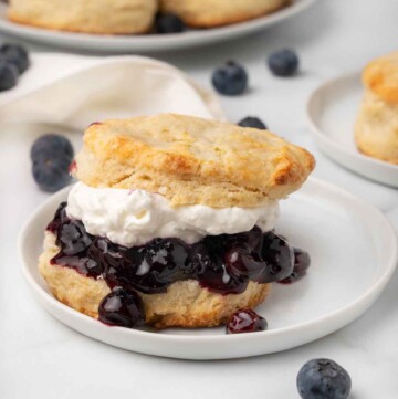 scone stuffed with blueberries and whipped cream on a white plate with scones in the background