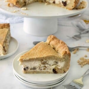 slice of torta di ricotta on a white plate with an other slice and the remainder of the cake in the backgroud