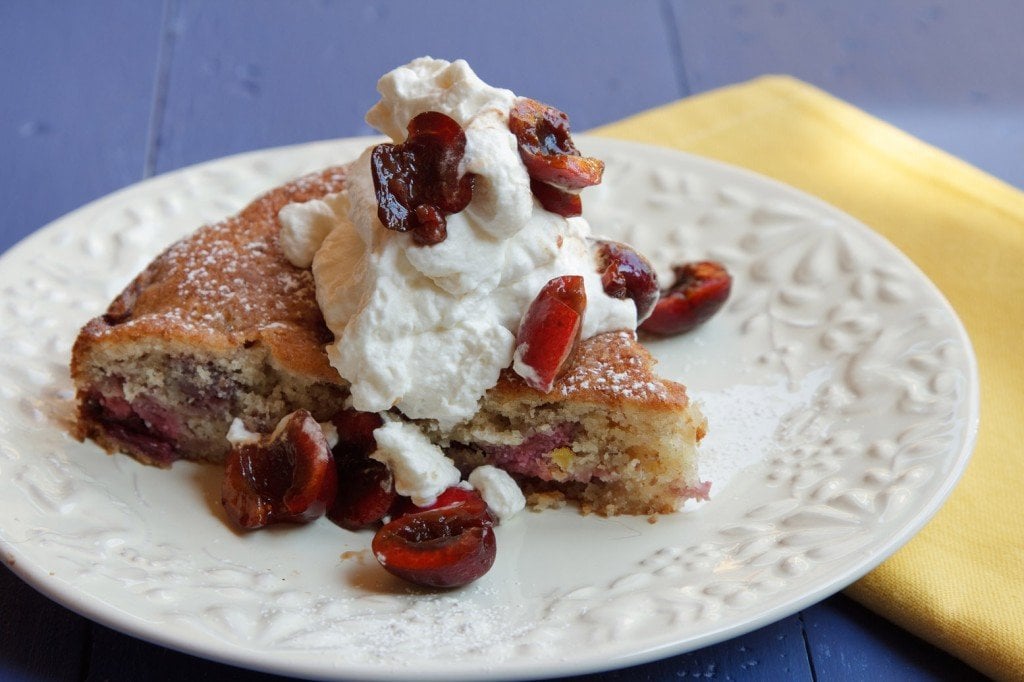 slice of cherry almond cake topped with whipped cream and cherries on a white plate