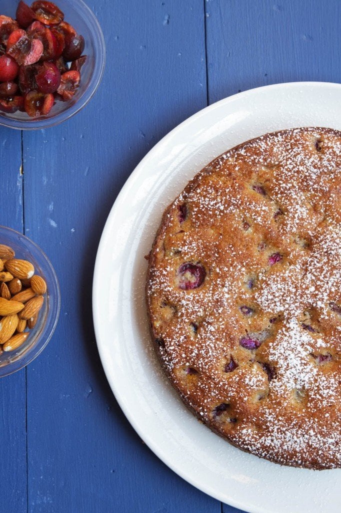 overhead partial view of cherry almond cake with bowls of cherries and almonds