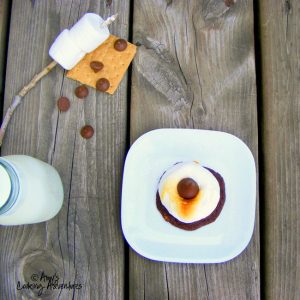 smores cookie on a white plate with marshmallows on a stick with graham crackers and chocolate next to it