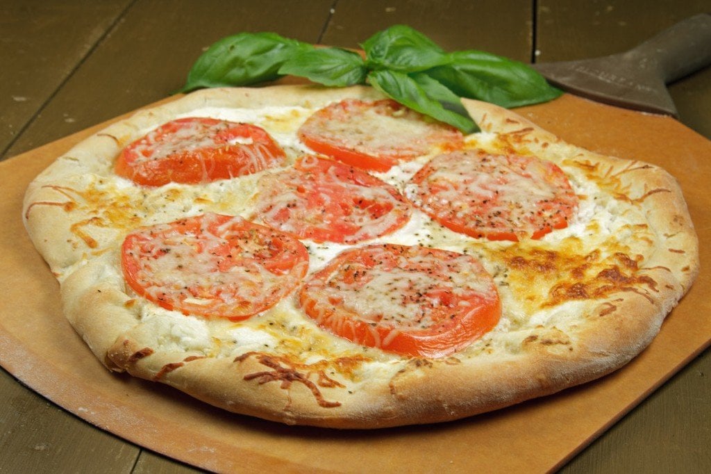 tomato ricotta pizza with a sprig of basil on a pizza peel