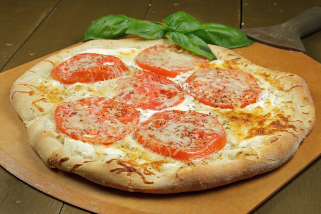 ricotta tomato pizza with a sprig on basil on a pizza peel