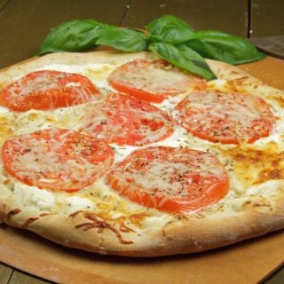 ricotta tomato pizza with a sprig on basil on a pizza peel