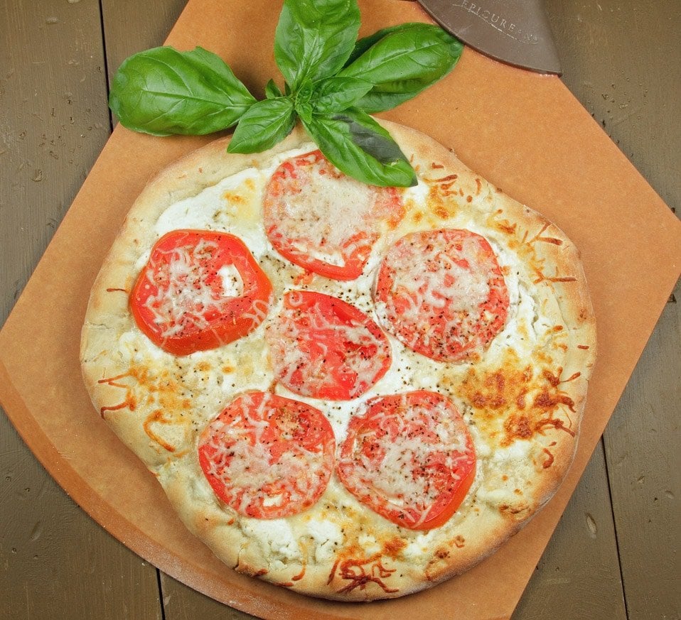 overhead view of tomato ricotta pizza with a sprig of basil on a pizza peel