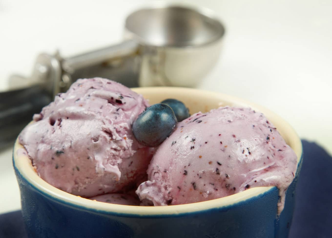 Blueberry Cheesecake with blueberries in a blue ramekin with a blurred ice cream scoop in the background