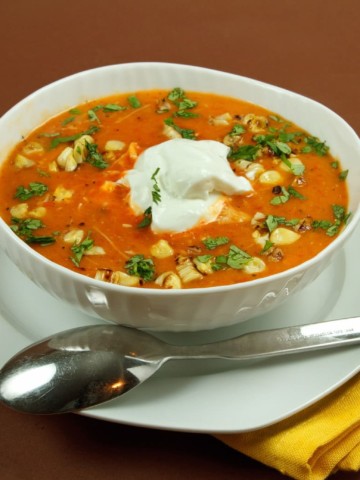 roasted red pepper soup in a white bowl on a white plate with a spoon