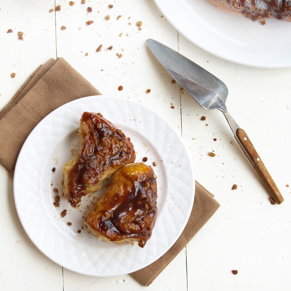 sticky buns on a white plate on top of a light brown napkin sitting on a white table with a spatula 