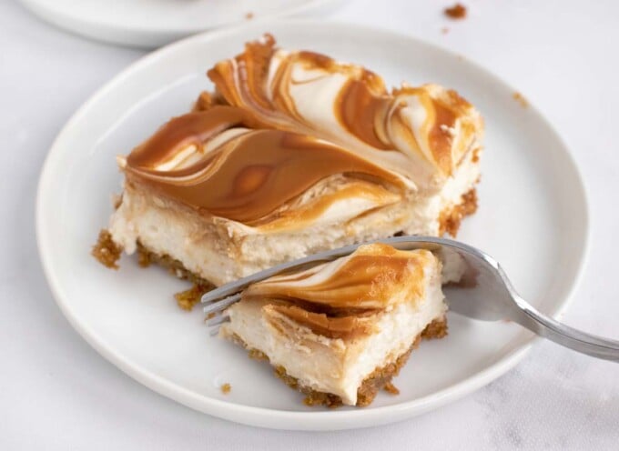 close up of biscoff cheesecake bar with a fork on a white plate