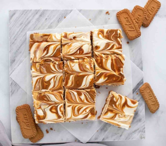 biscoff cheesecake bars sliced intro squares next to biscoff cookies on a white marble tray