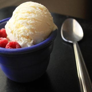 scoop of lemon curd ice cream in a blue bowl with berries and a spoon next to it