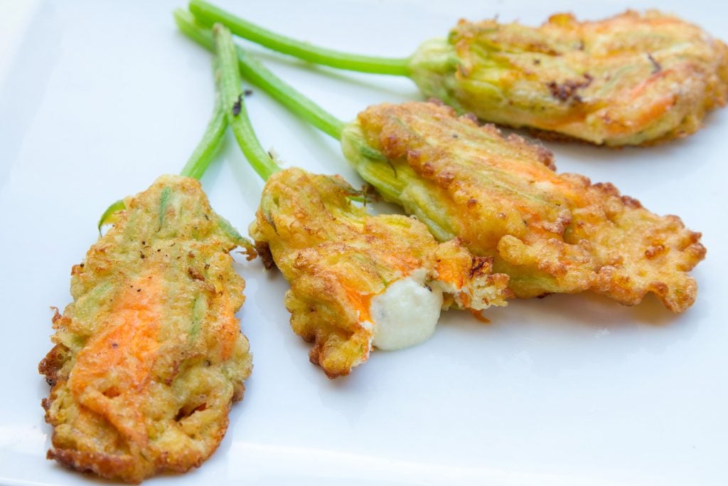 4 squash blossoms on a white plate, one with a bite out of it
