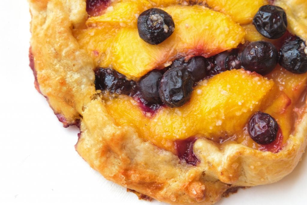 partial view of a blueberry peach crostata on a white plate