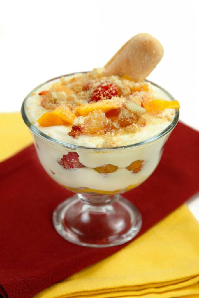 peach tiramisu with raspberries in a glass dish on a red and yellow napkin