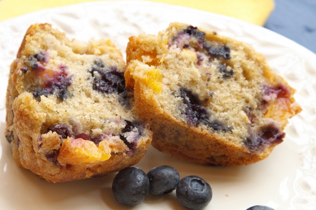 split nectarine blueberry muffin sitting on a white plate on a yellow napkin 