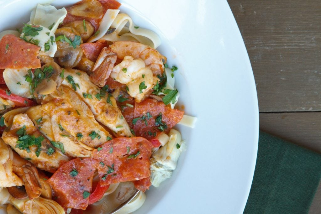 chicken and shrimp pepperoni in a white bowl on a brown table with a dark green napkin