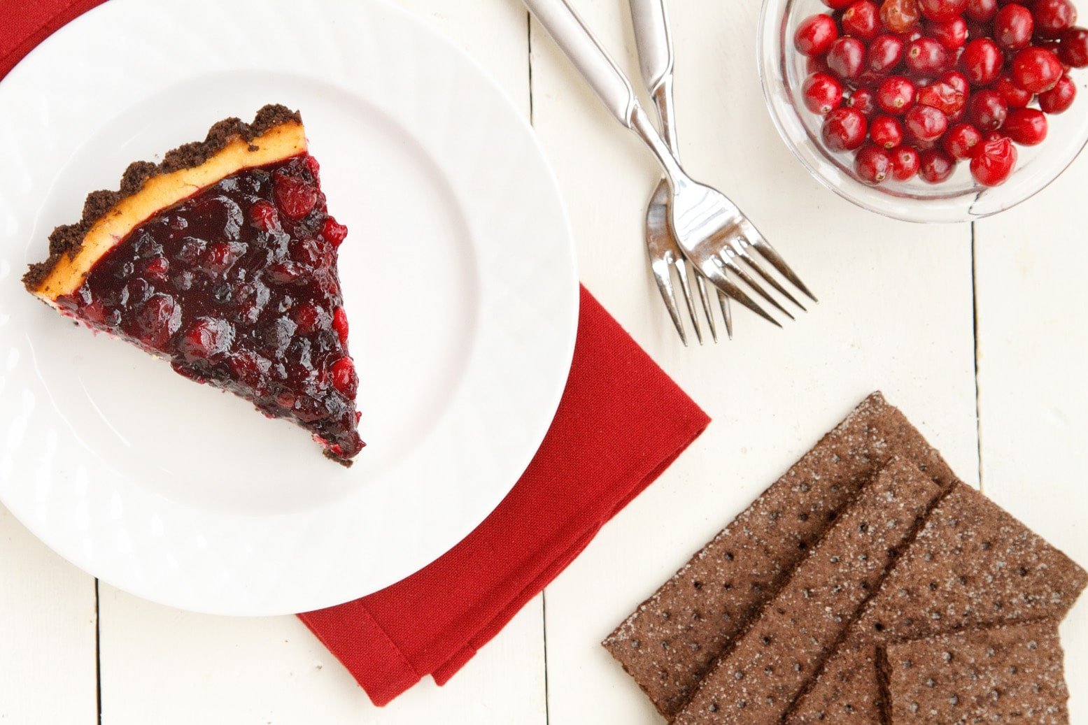 overhead view of a slice of amethyst cheesecake on a white plate with 2 forks and red napkin