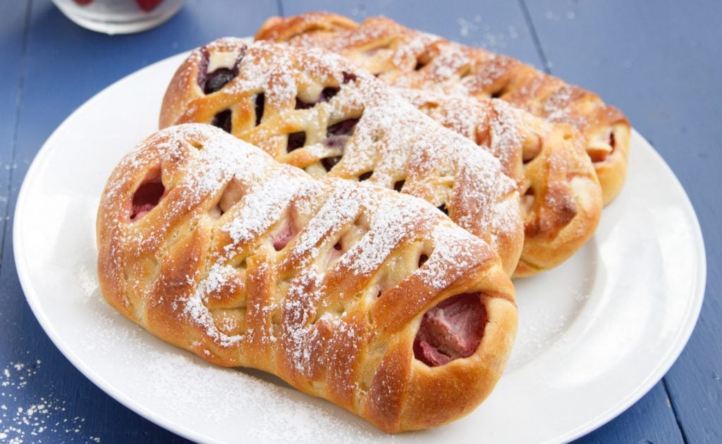  brioche dough danish on a white plate sitting on a blue table sprinkled with powdered sugar