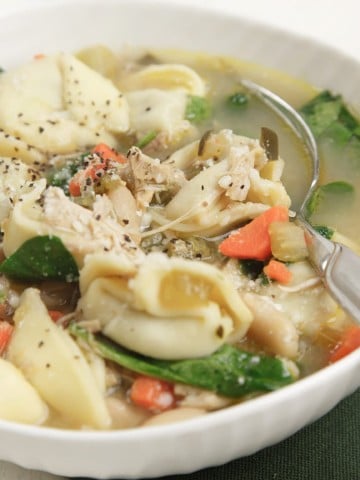 white bowl with sausage and tortellini soup with a spoon
