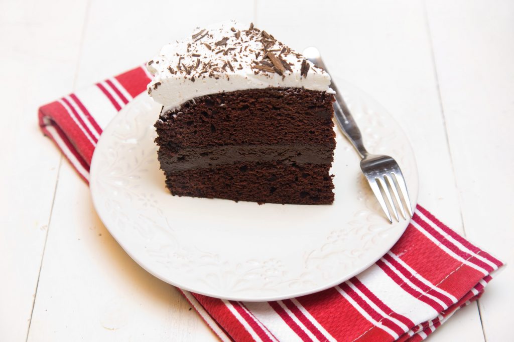 slice of Chocolate Fudge Cake with Whipped Cream on a white plate on a red and white striped napkin