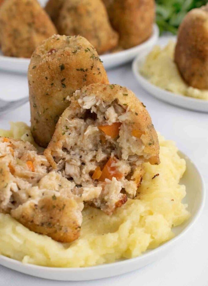 turkey croquettes with one split open on a bed of mashed potatoes on a white plate