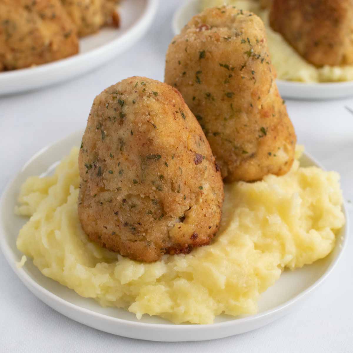 two croquettes on a a bed of mashed potatoes on a white plate