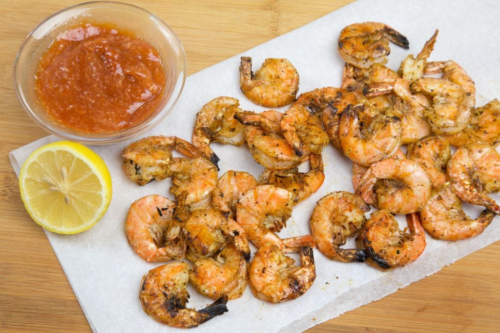 grilled u-peel shrimp on white paper with a half a lemon and bowl of cocktail sauce