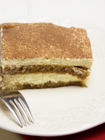 a slice of tiramisu with a dusting of cocoa sitting on a white plate with a fork on the plate