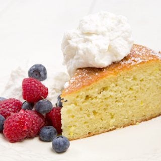 slice of orange yogurt cake with berries and whipped cream on a white plate