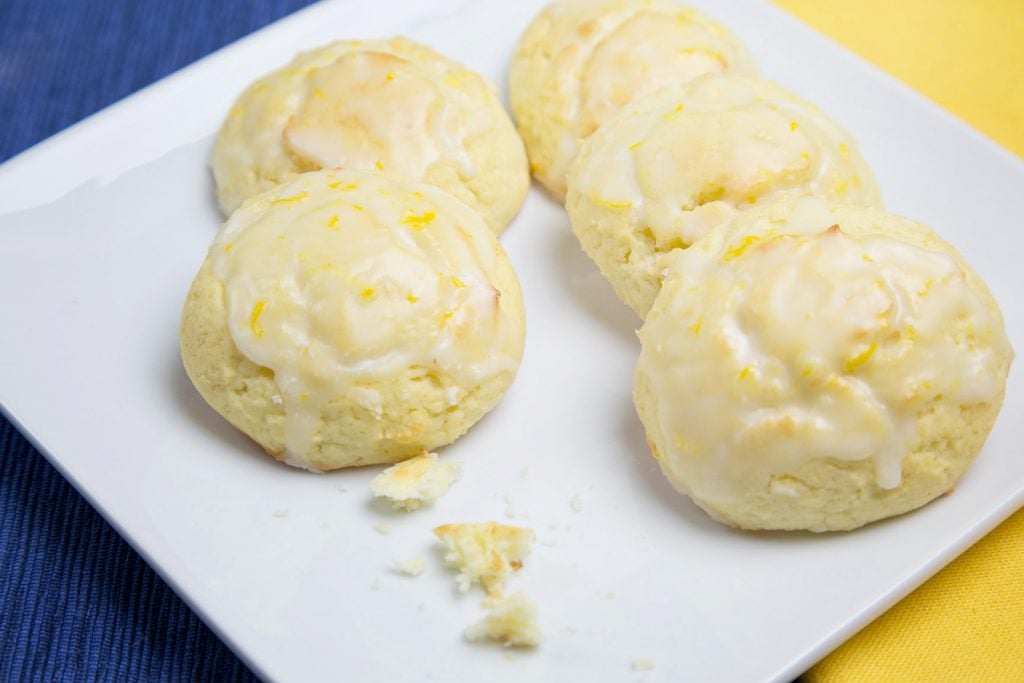 a white plate with 5 ricotta lemon cookies and crumbs from one that was eaten