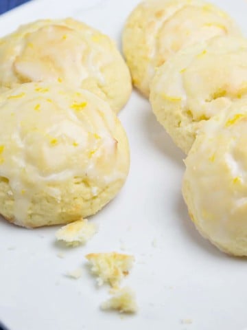 a white plate with 5 ricotta lemon cookies and crumbs from one that was eaten