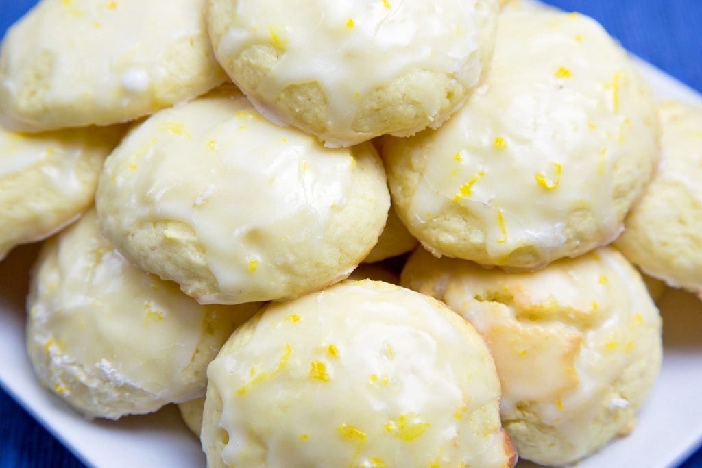 meyer lemon ricotta cookie with a lemon glaze on a white plate with a blue background