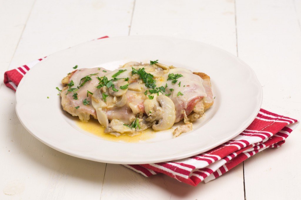 side view of Chicken Sorrento garnished with parsley on a white plate sitting on top of a red and white striped napkin