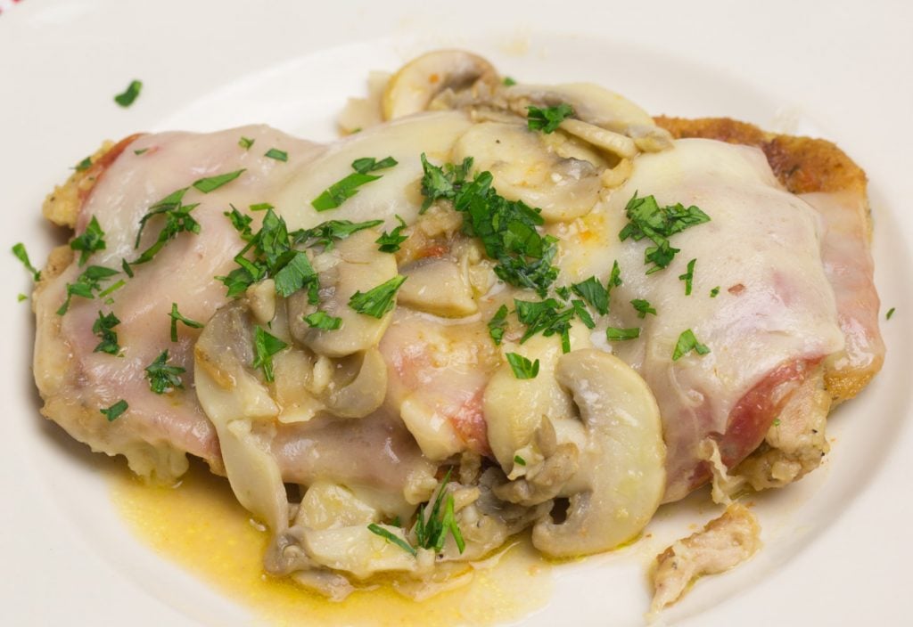side view of Chicken Sorrento garnished with parsley and mushrooms on a white plate