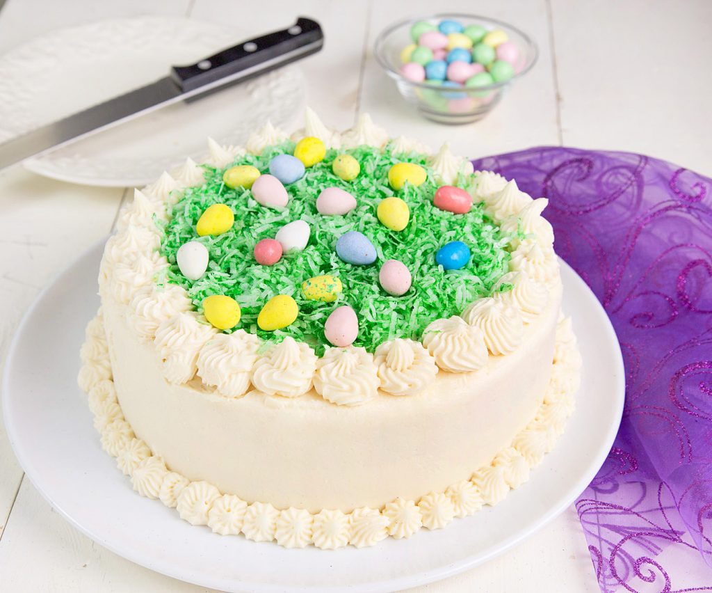 whole coconut easter cake on a white platter with a purple chiffon napkin