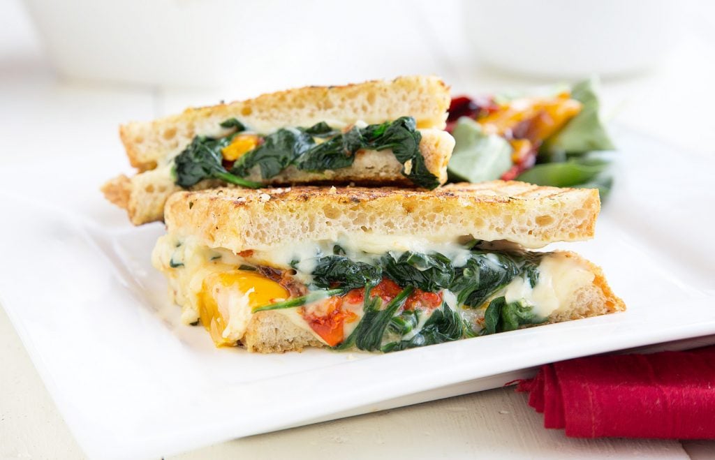 side view of Italian Grilled Cheese with roasted peppers and spinach on a white plate