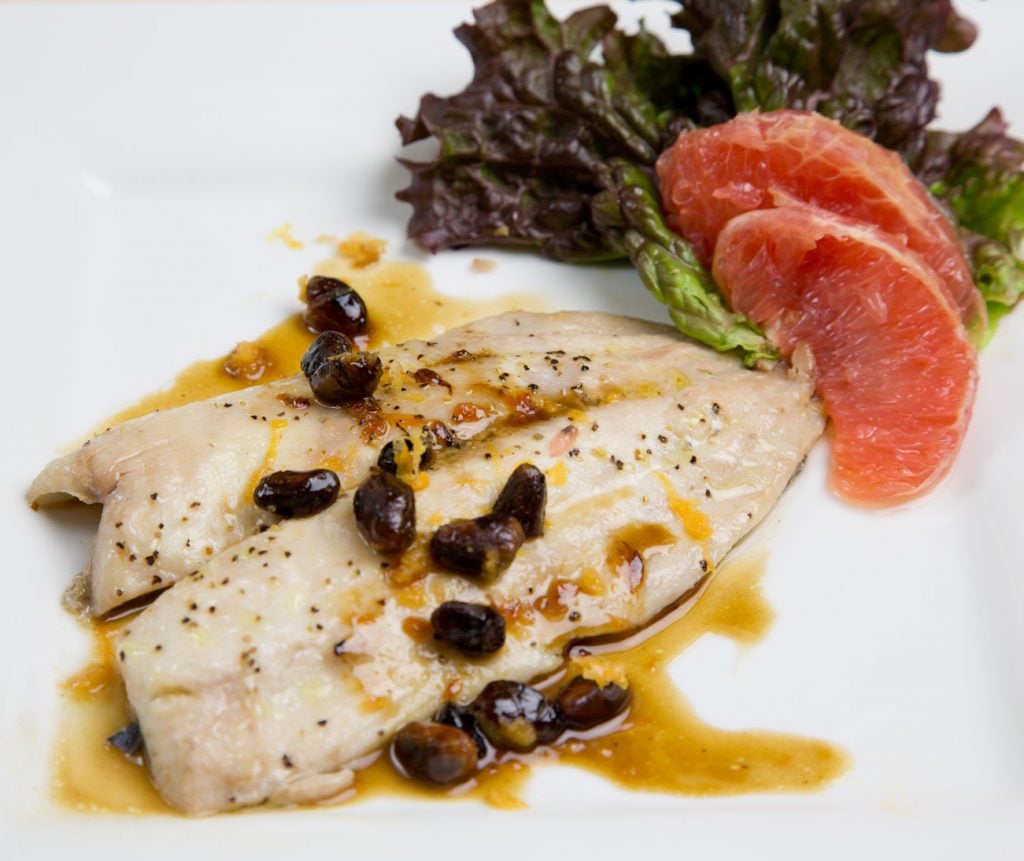 roasted Florida Pompano on a white plate with pistachios in a sauce with sliced grapefruit and red leaf lettuce on the side