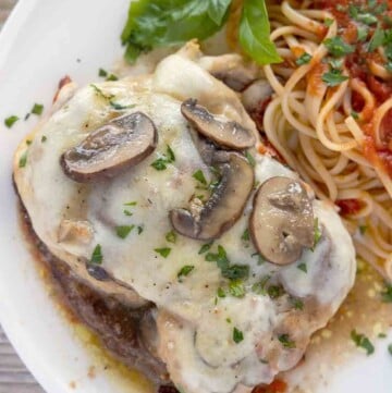 chicken sorrento on a white plate with a sprig of basil and linguine with red sauce