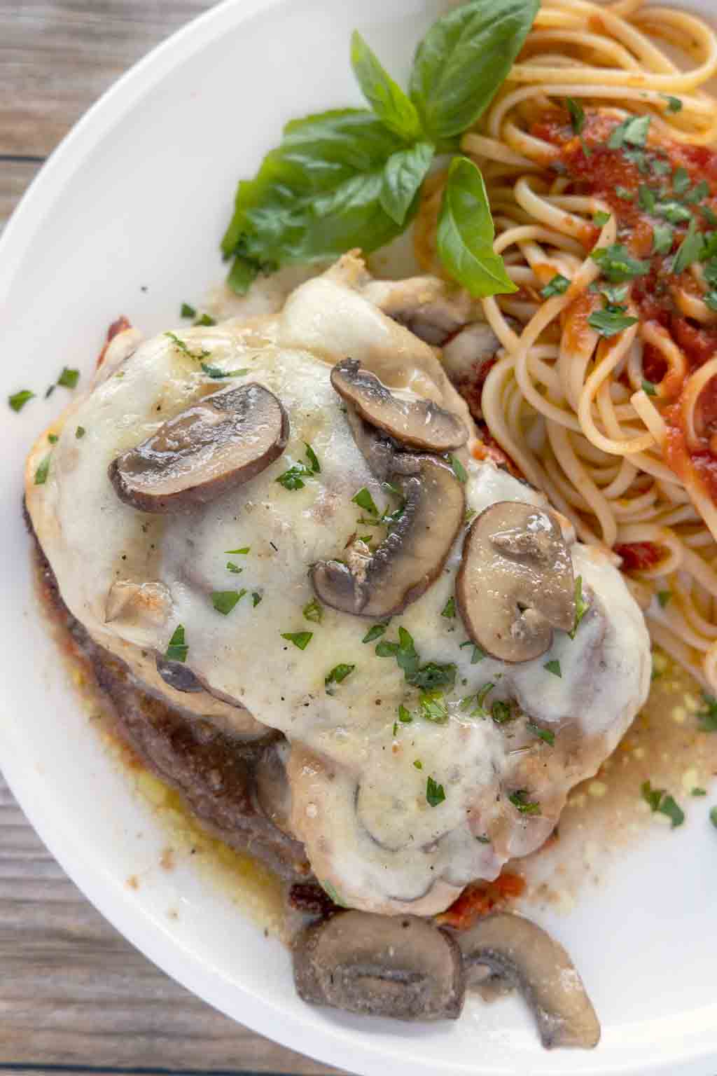 chicken sorrento on a white plate with a sprig of basil and linguine with red sauce