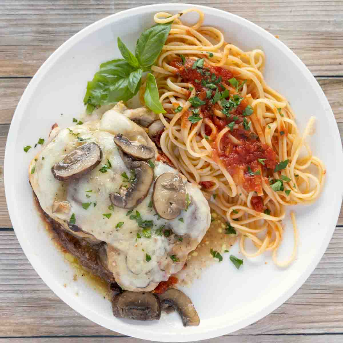 chicken sorrento on a white plate with a sprig of basil and linguine with red sauce