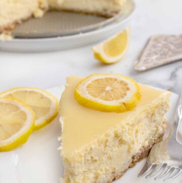 slice of lemon cheesecake on a white plate with sliced lemons and a fork