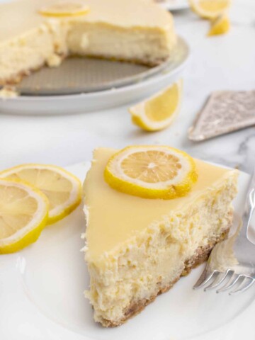 slice of lemon cheesecake on a white plate with sliced lemons and a fork